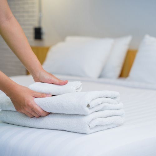 Person arranging folded towels on a neatly made vacation rental bed