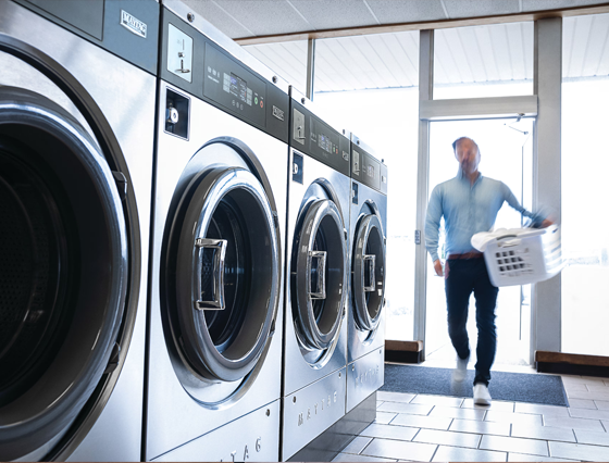 Man walking through a commercial laundry room with multiple washing machines for large laundry loads